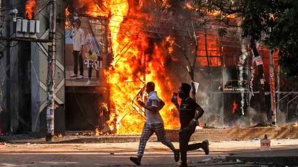 Men run past a Dhaka shopping center set on fire by protesters during a rally against Bangladeshi&nbsp;Prime Minister Sheikh Hasina&nbsp;on Aug. 4.