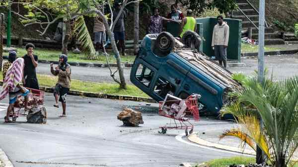 People gather near an overturned car&nbsp;in Noumea,&nbsp;New Caledonia, on May 16. France says TikTok posts and the Central Asian nation of Azerbaijan are fanning the violence in New Caledonia.